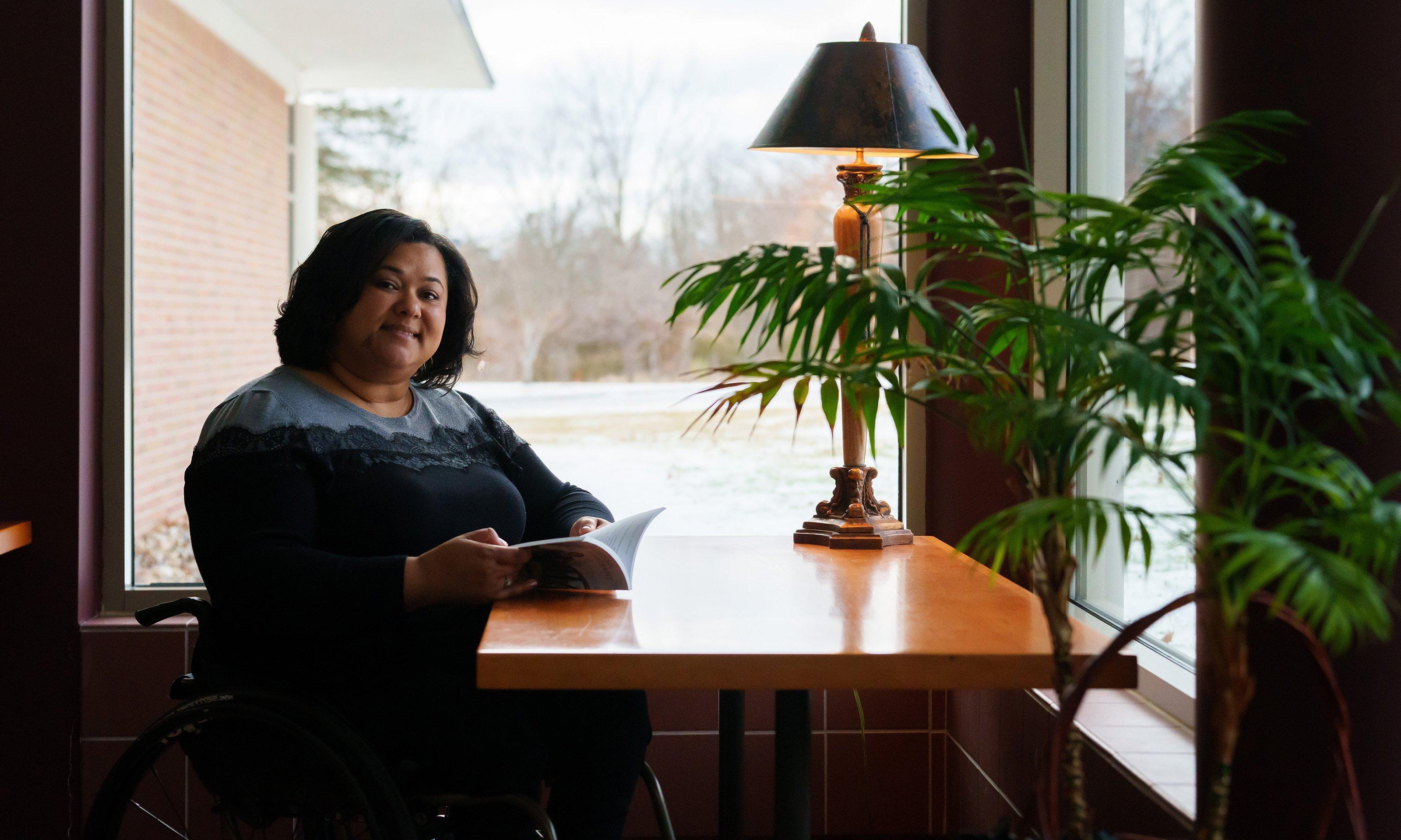 A woman at a desk in front of a window, reading a book