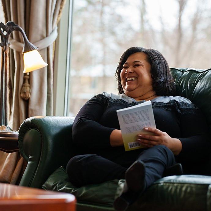 A woman sitting in a chair, holding a book and laughing